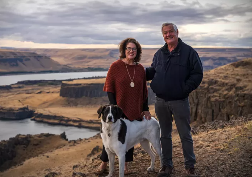 A man and a woman are standing next to a dog on top of a hill.