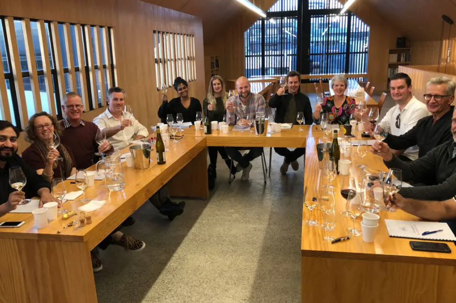 A group of people are sitting at a long table drinking wine.