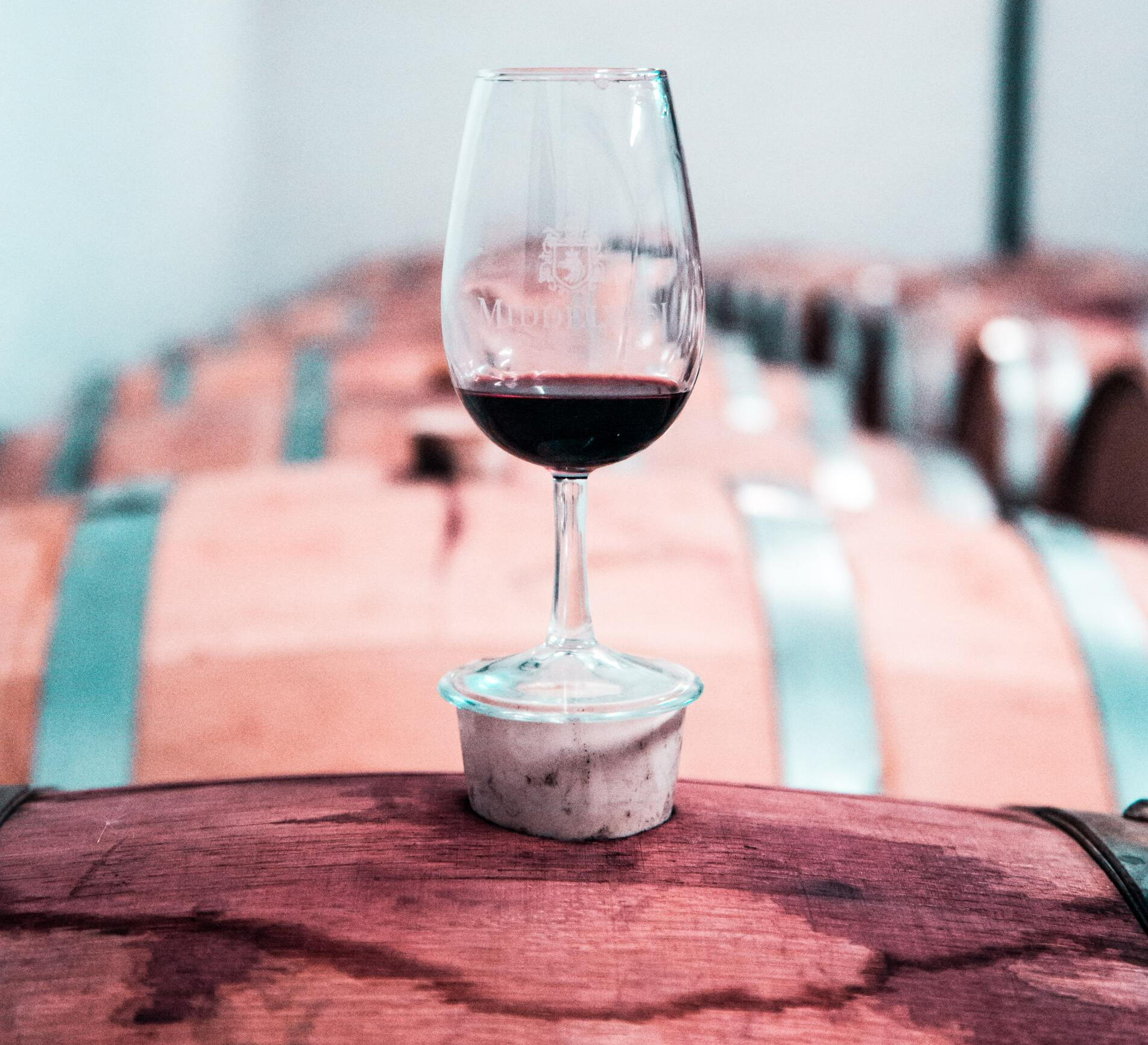 A glass of red wine is sitting on top of a wooden barrel.