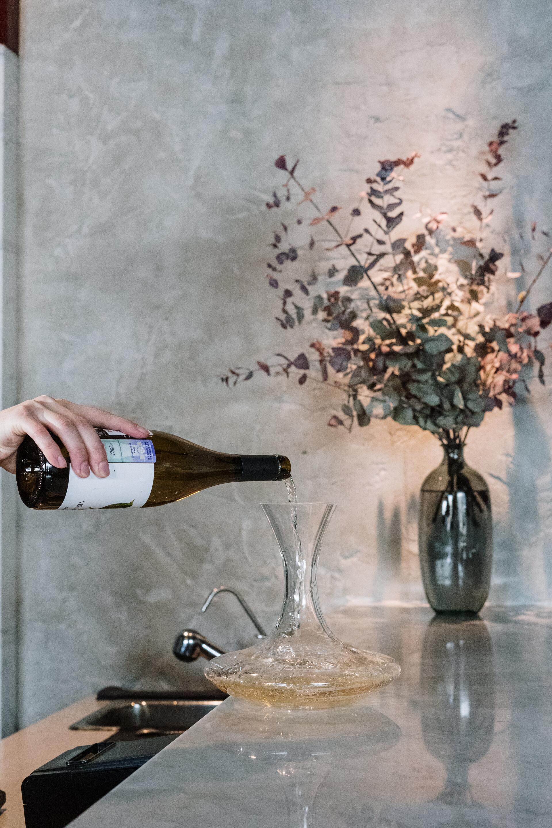 A person is pouring a bottle of wine into a decanter.