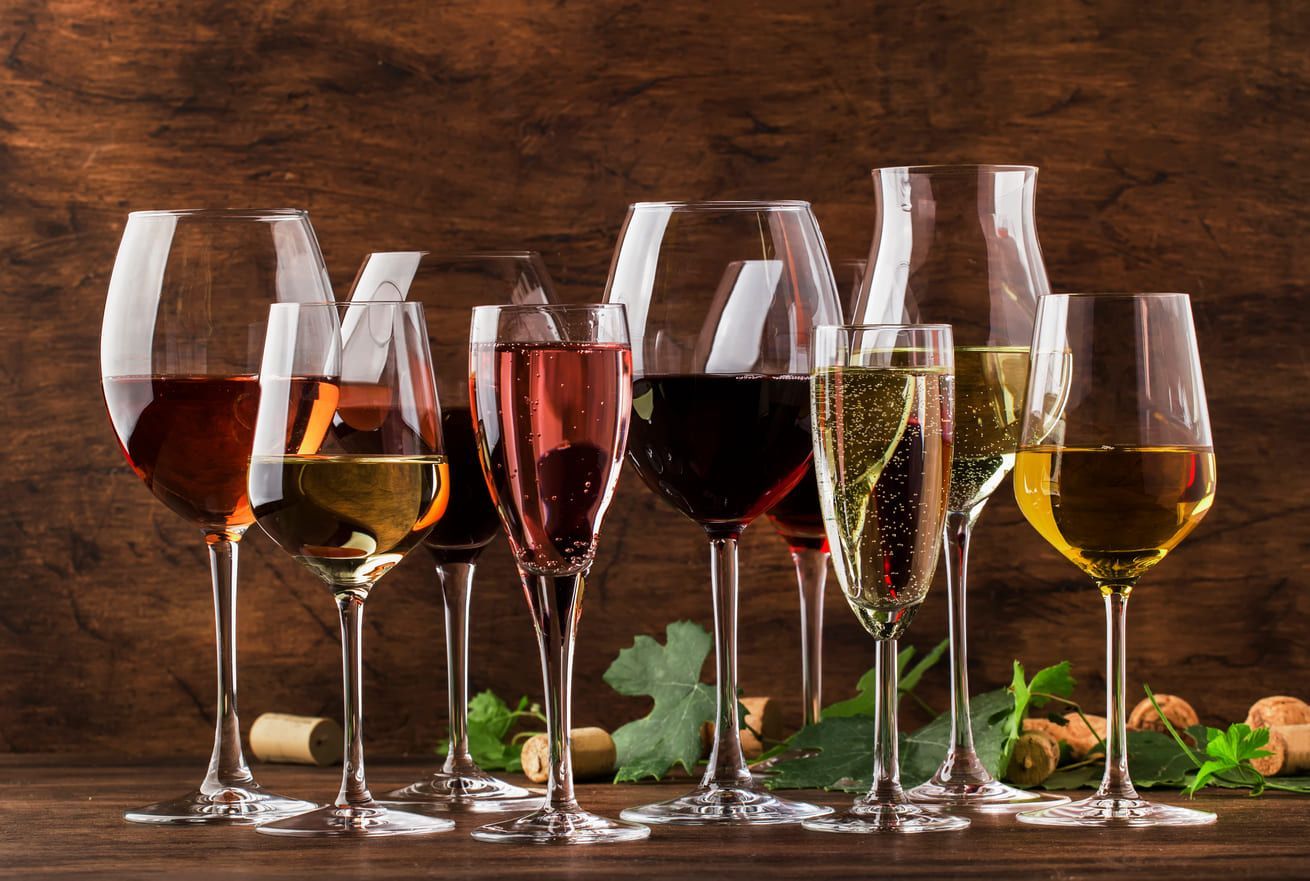 A row of wine glasses filled with different types of wine on a wooden table.
