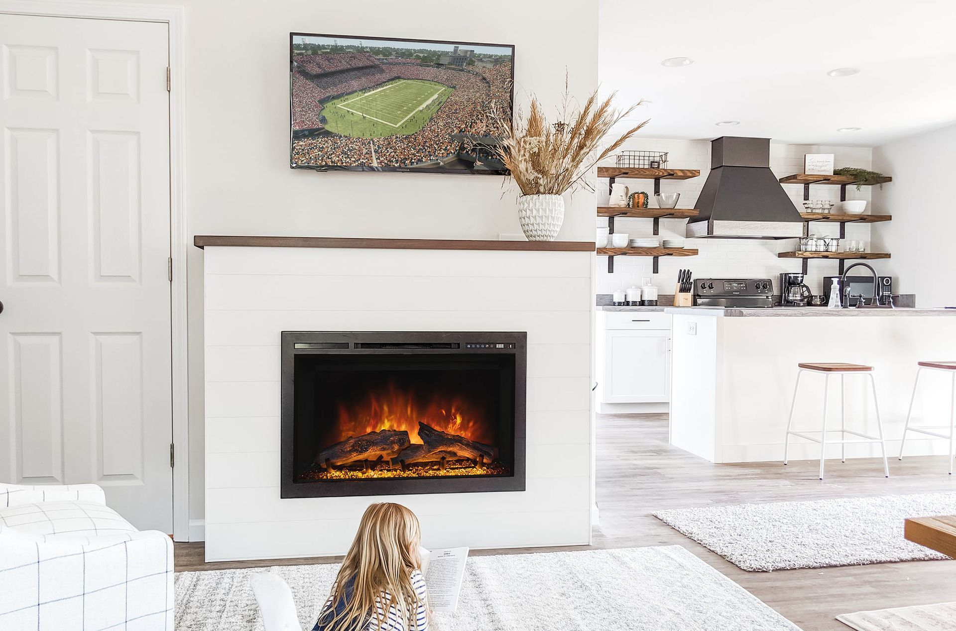 Cozy living room with a fireplace and TV; a child sits on the rug, facing the fireplace.