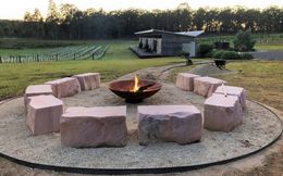 Fire pit with sandstone seats in a circle, with vineyard and building in the background.