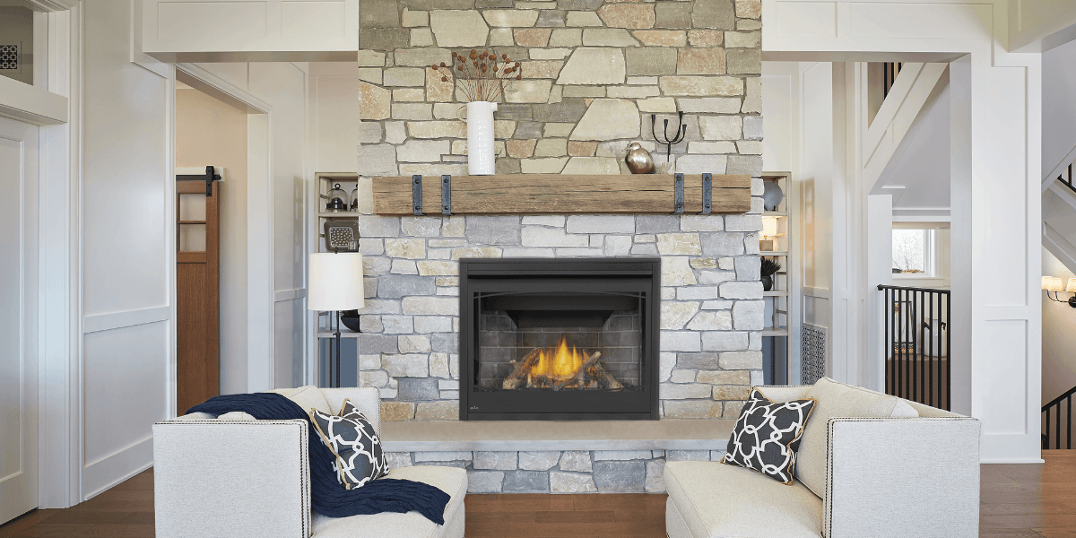 Cozy living room with stone fireplace, lit fire, white armchairs with patterned pillows.