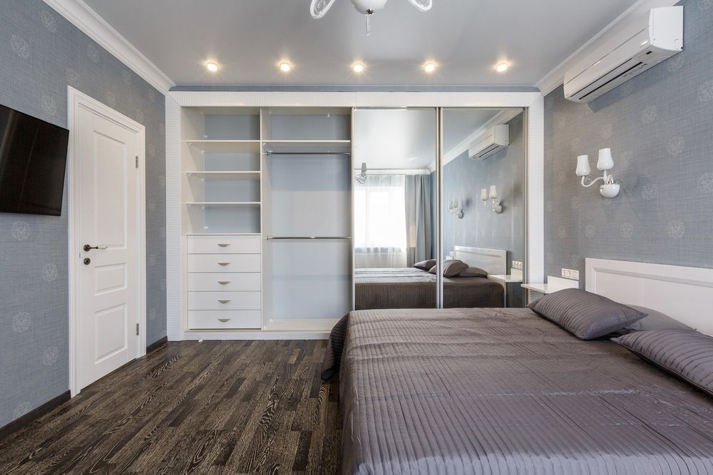 A bedroom with a sliding door wardrobe filled with drawers and shelves.