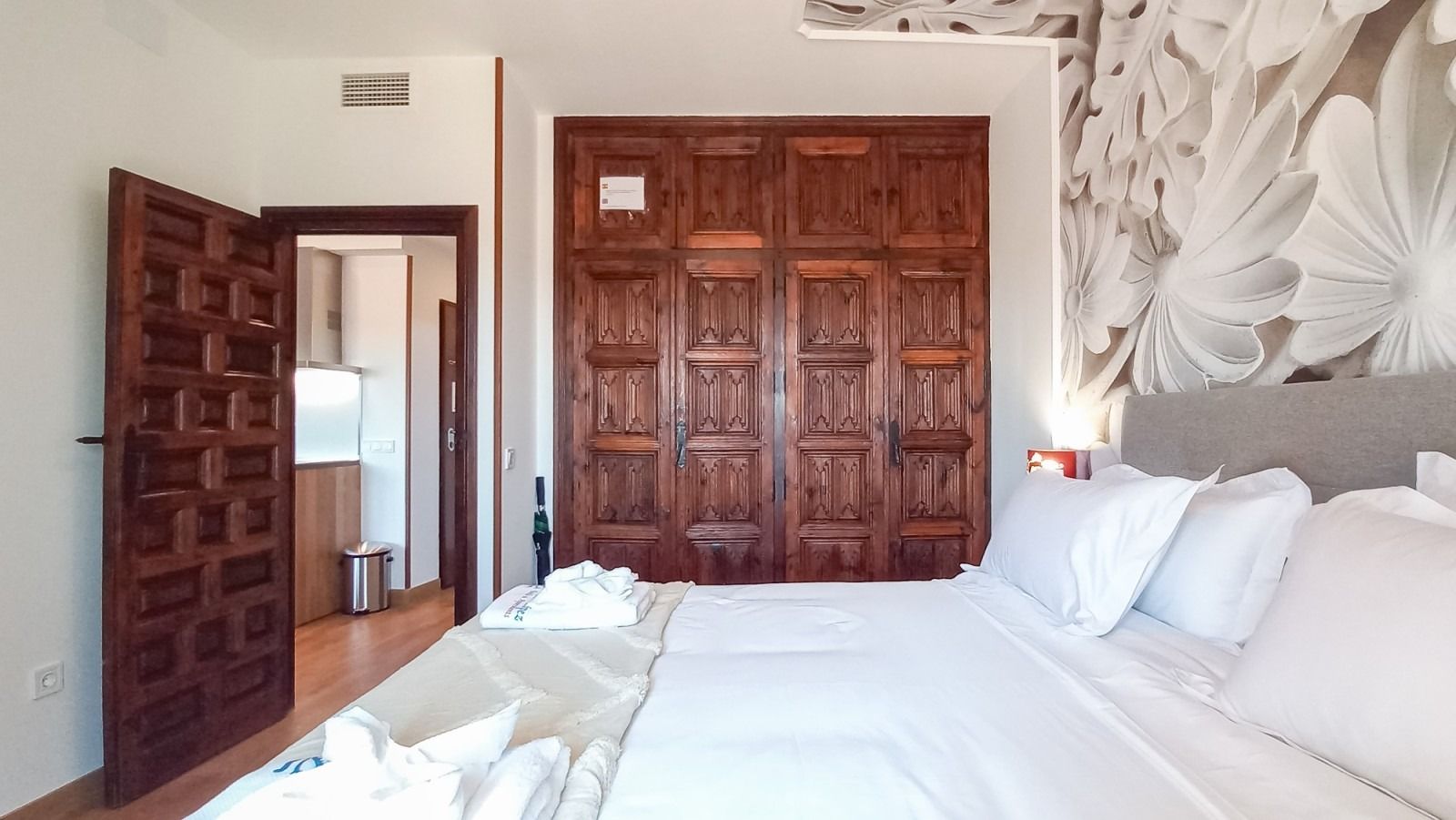 Dormitorio con gran armario de madera, cama, puerta abierta a cocina americana.