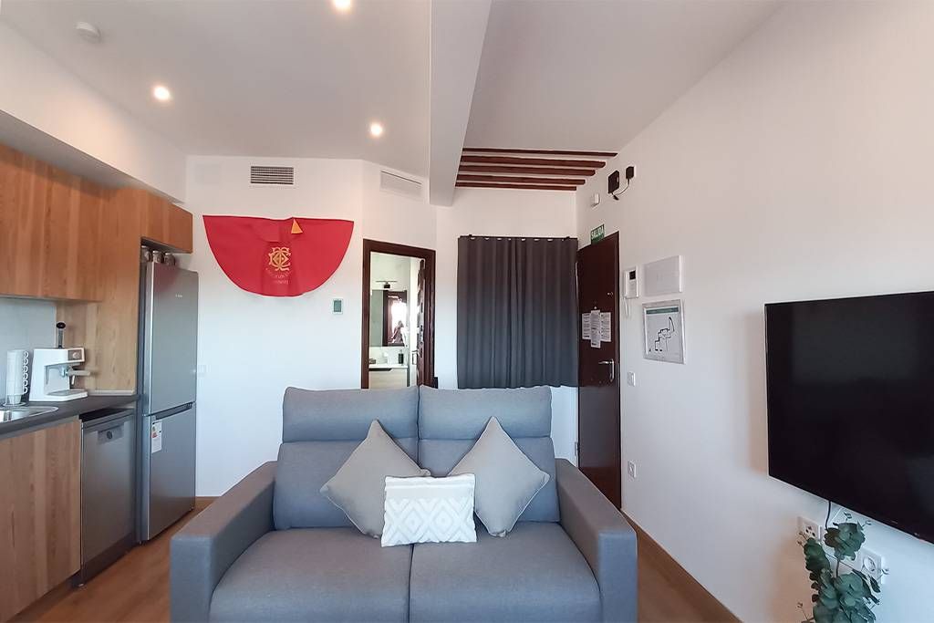 Sala de estar con sofá gris, cocina, TV y una puerta al baño.
