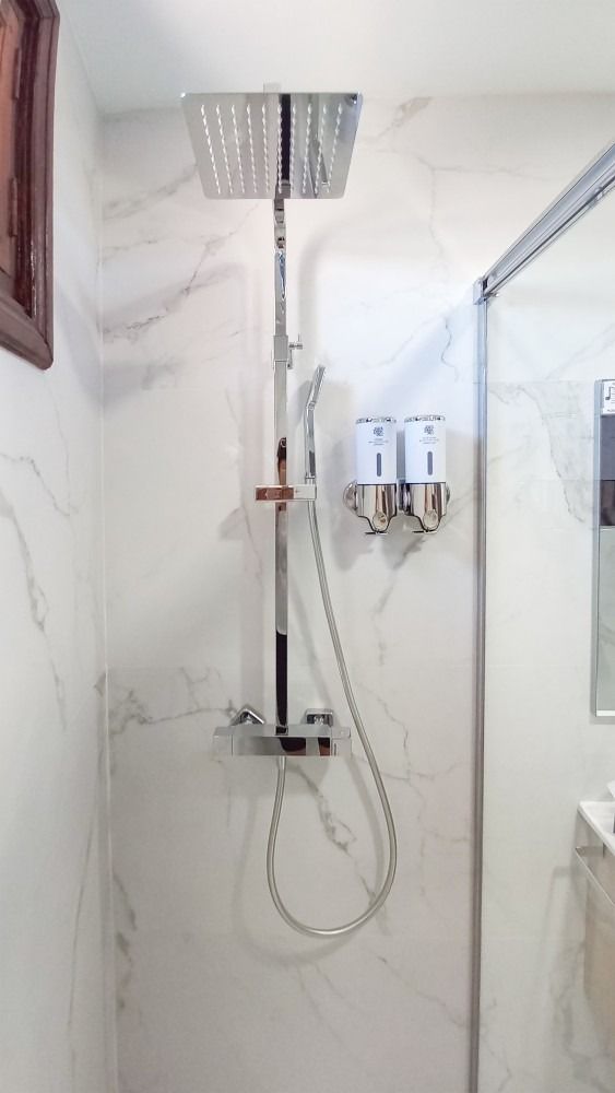 Ducha con rociador de lluvia, teleducha y paredes de azulejos efecto mármol. Dispensadores de jabón integrados.