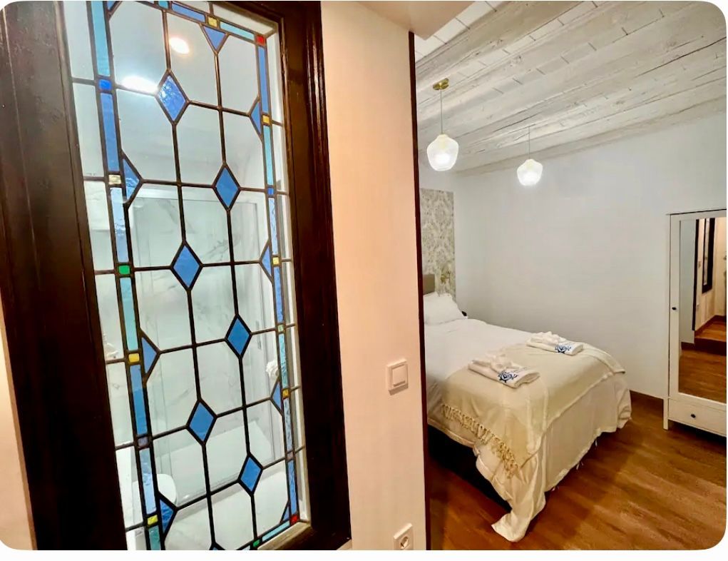 Vidriera que da a un dormitorio con cama blanca y suelo de madera.