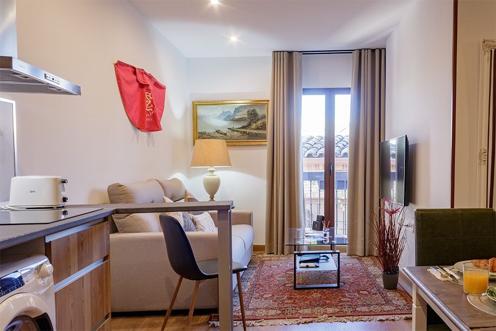 Acogedora sala de estar en apartamento con sofá, ventana, obras de arte y cocina pequeña.
