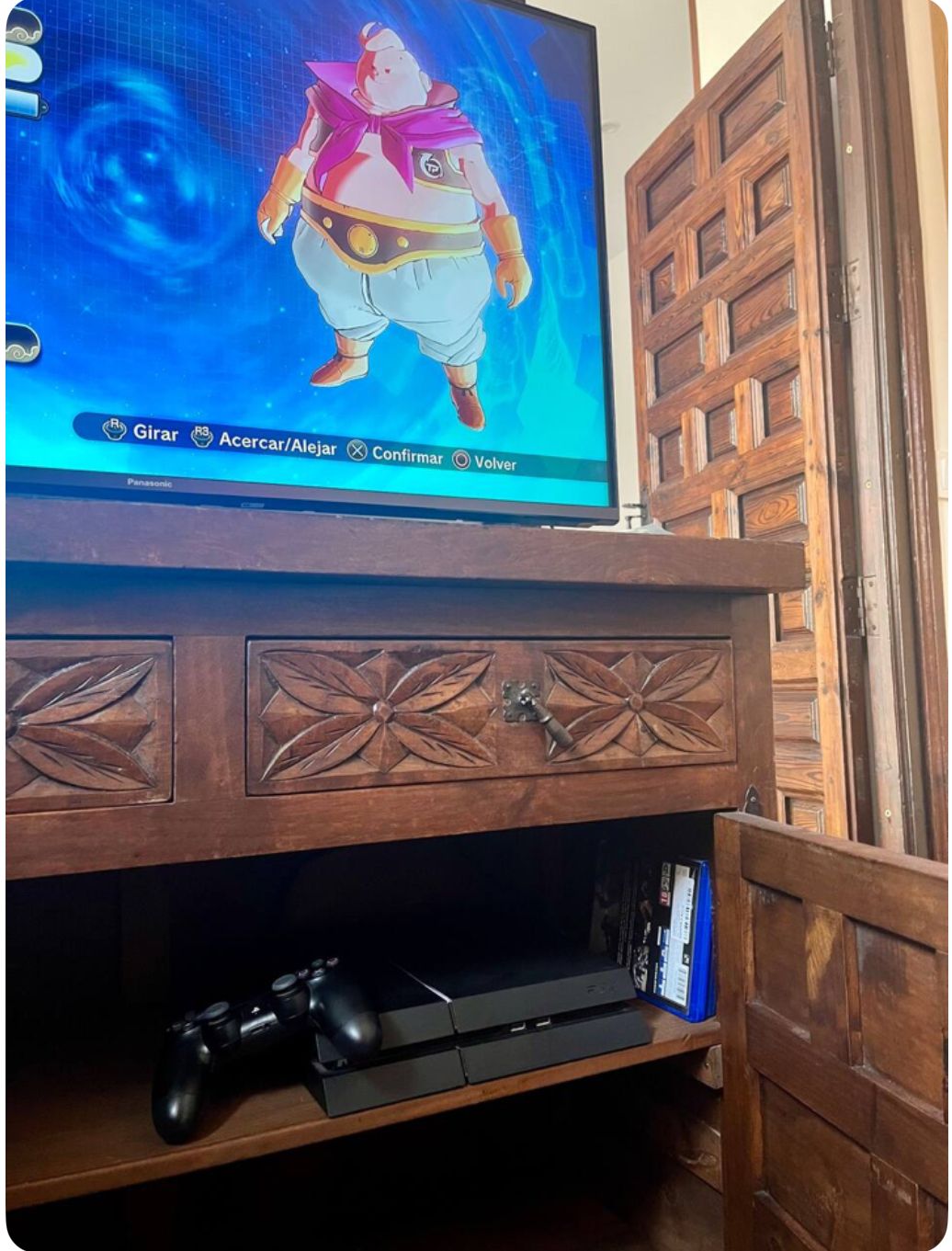 Una consola PlayStation 4 y un controlador se encuentran sobre un gabinete de madera con un televisor que muestra un personaje de videojuego.