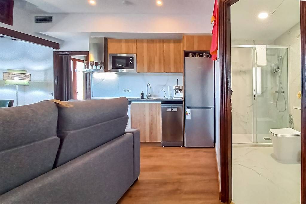Zona de estar con sofá, cocina con electrodomésticos y un baño visible a través de una puerta abierta.