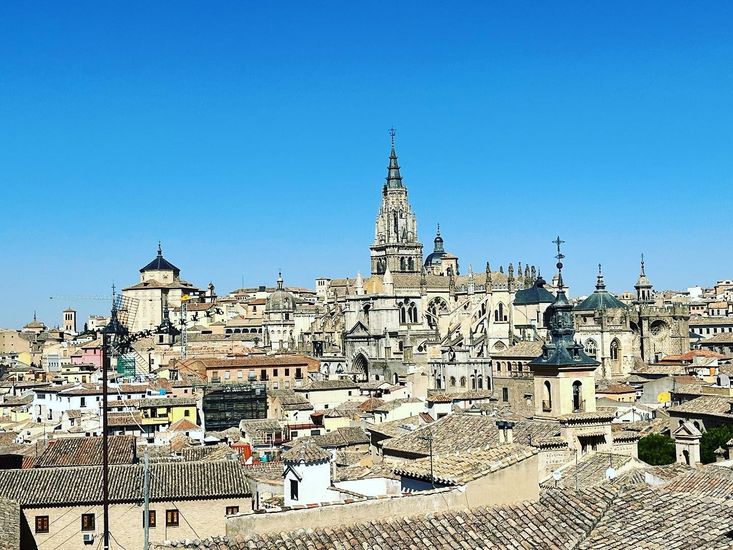 Paisaje urbano de Toledo, España, con una gran catedral y numerosos edificios bajo un cielo azul.