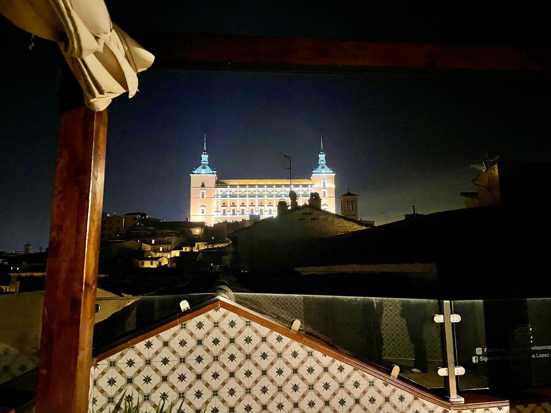 Vista nocturna de Toledo, España, con la fortaleza del Alcázar iluminada al fondo, vista por encima de los tejados.