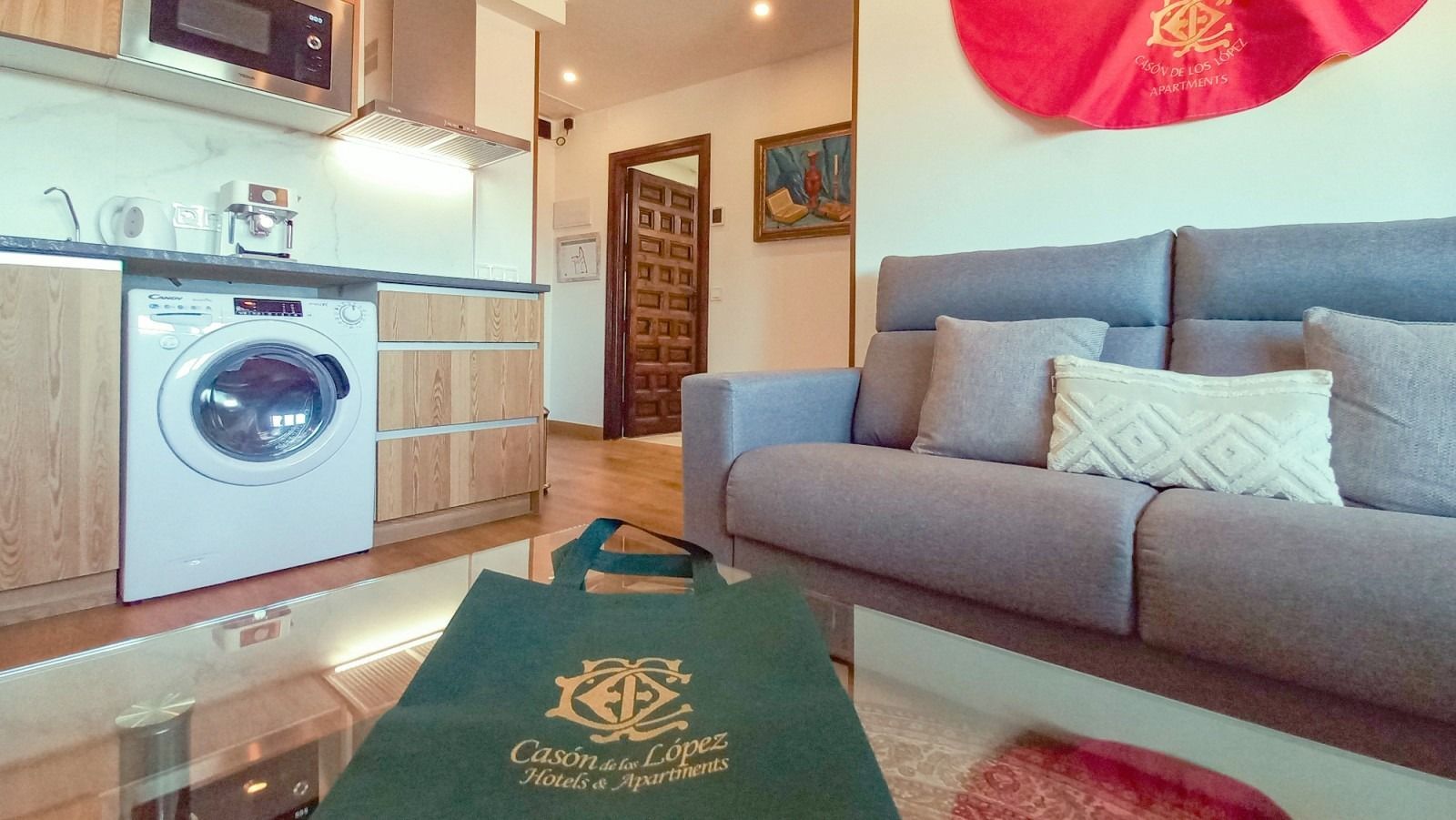 Cocina y sala de estar con un sofá gris, gabinetes de madera y lavadora.