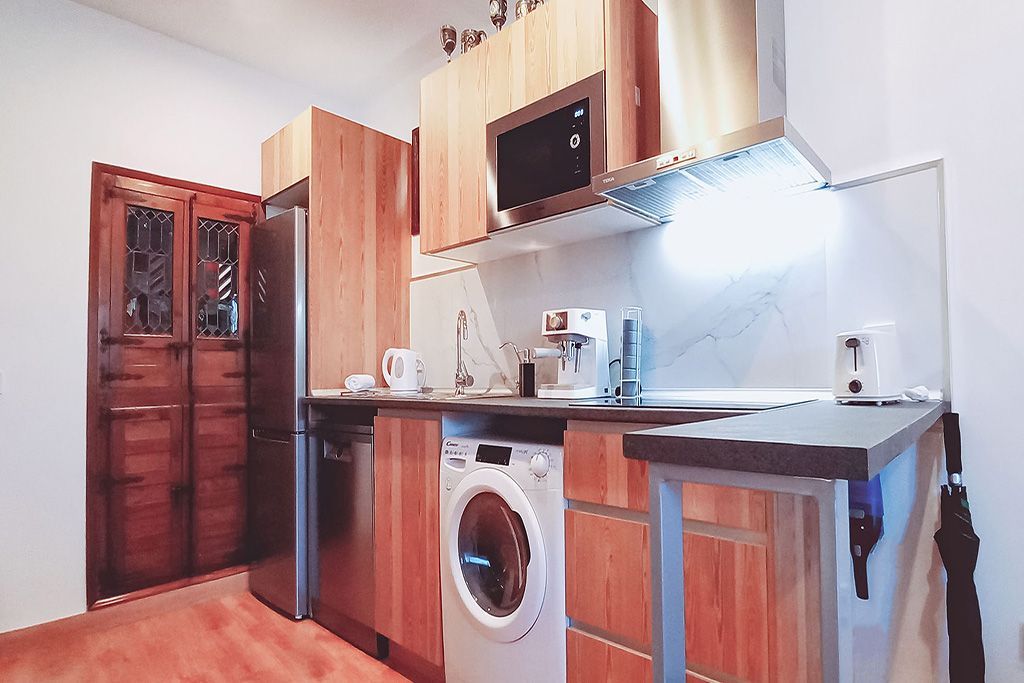 Pequeña cocina con gabinetes de madera, electrodomésticos de acero inoxidable y lavadora.