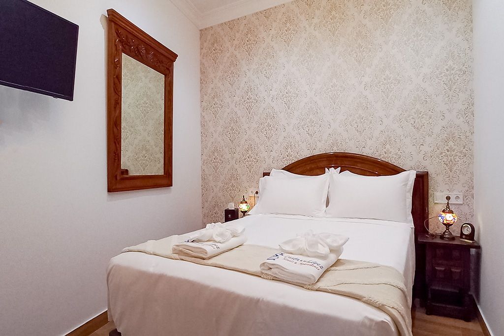 Acogedor dormitorio con una cama doble, cabecera de madera adornada y una pared con textura rústica detrás.