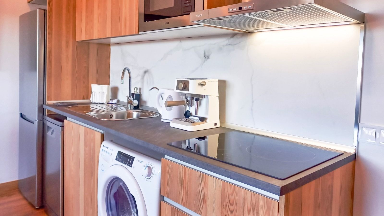 Cocina con muebles de madera, electrodomésticos de acero inoxidable y lavadora.