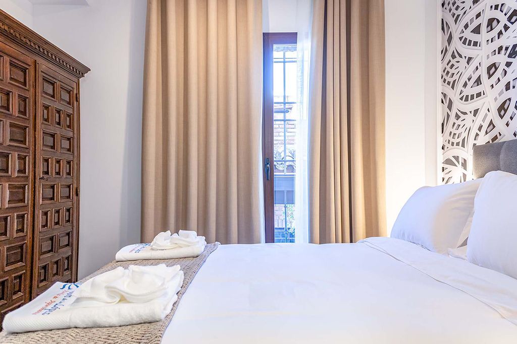 Dormitorio con cama, cabecero estampado, armario de madera y cortinas color canela sobre una puerta abierta.