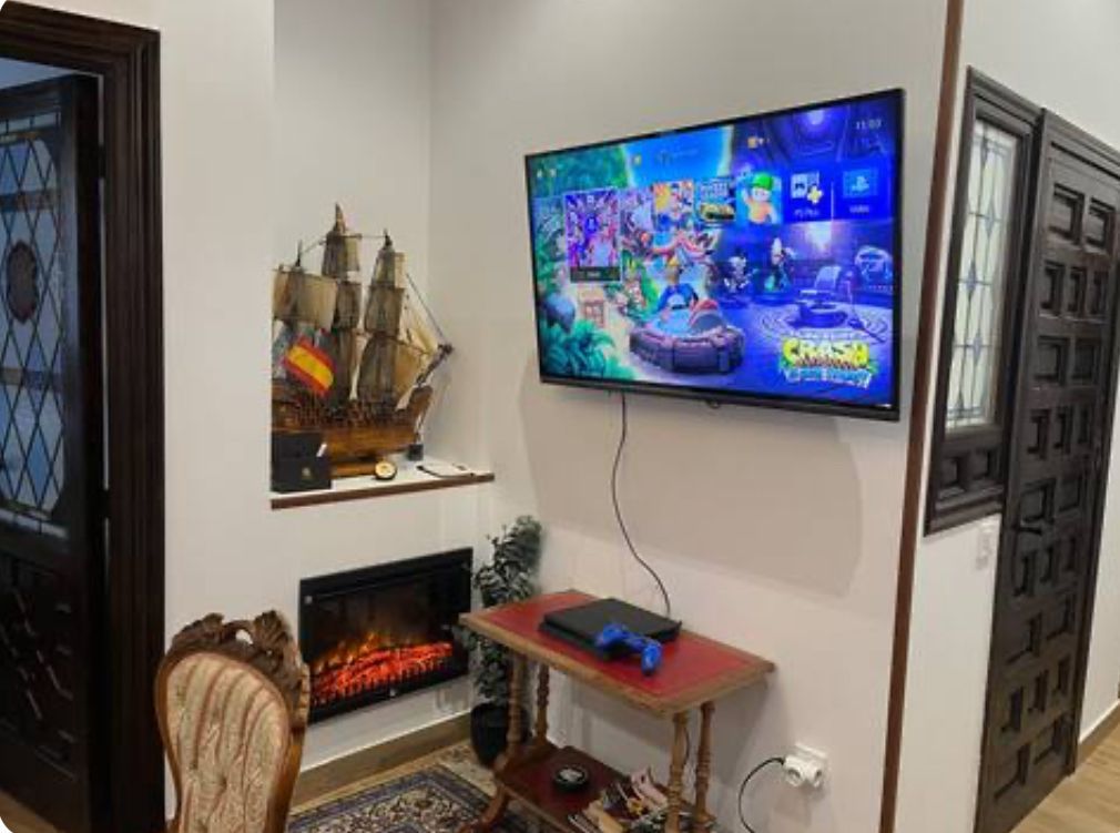Sala de juegos: Televisor con pantalla de juegos sobre una mesita con consola. Chimenea decorativa y barco.