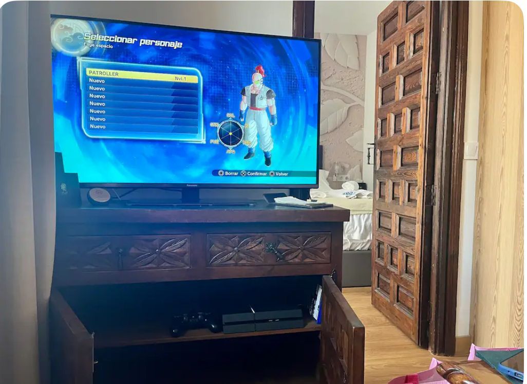 Un televisor muestra un juego de Dragon Ball en un mueble de madera con una puerta abierta cerca.