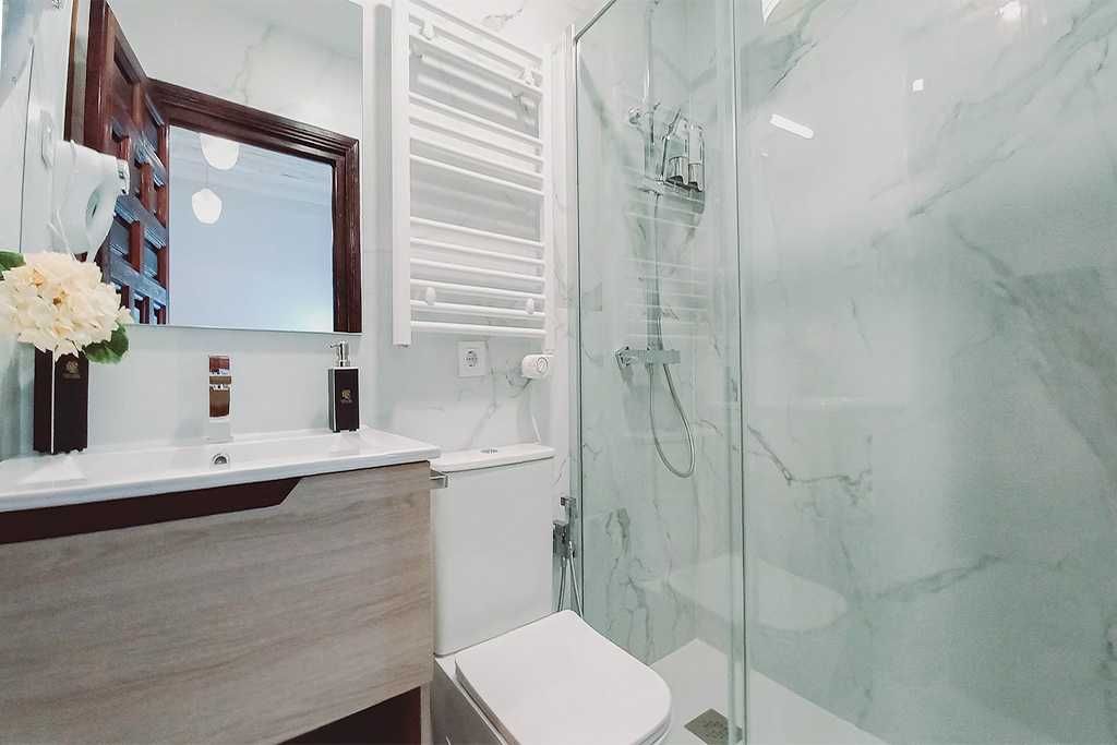 Baño moderno con paredes con estampado de mármol, ducha de cristal, inodoro, tocador y una ventana con vista.