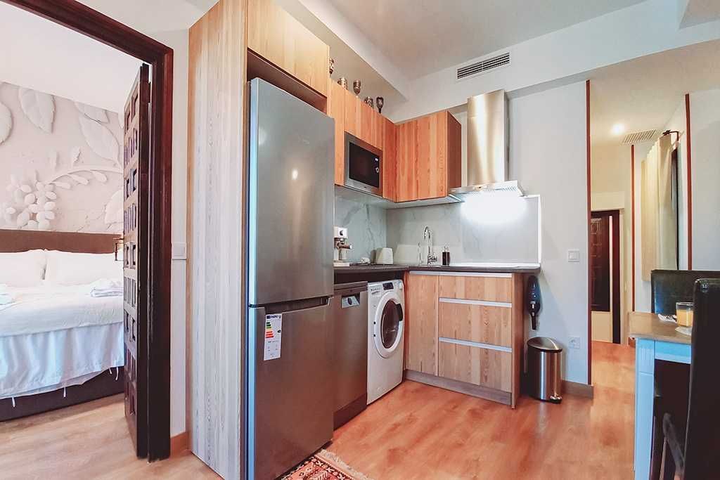 Cocina con gabinetes de madera, electrodomésticos de acero inoxidable y vista a un dormitorio y al comedor.