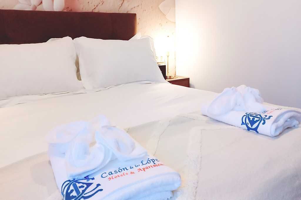 Cama blanca con toallas dobladas y una lámpara de noche.