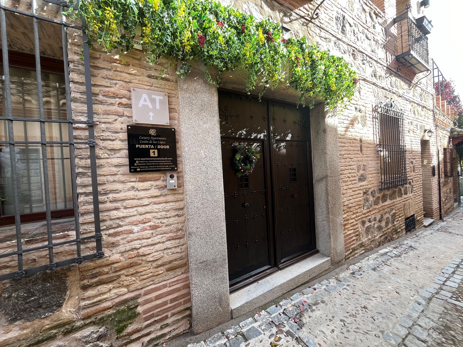 Un edificio de ladrillo con una puerta de madera decorada con vegetación; un pequeño cartel dice 