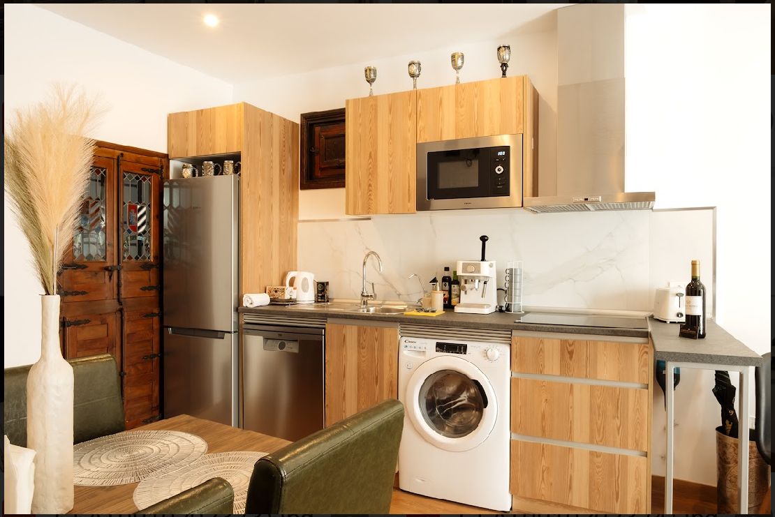 Pequeña cocina con gabinetes de madera, electrodomésticos de acero inoxidable y lavadora.