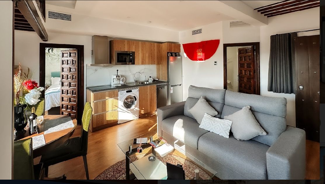 Acogedor apartamento con sala, cocina y comedor. Sofá gris, armarios de madera y obras de arte rojas.