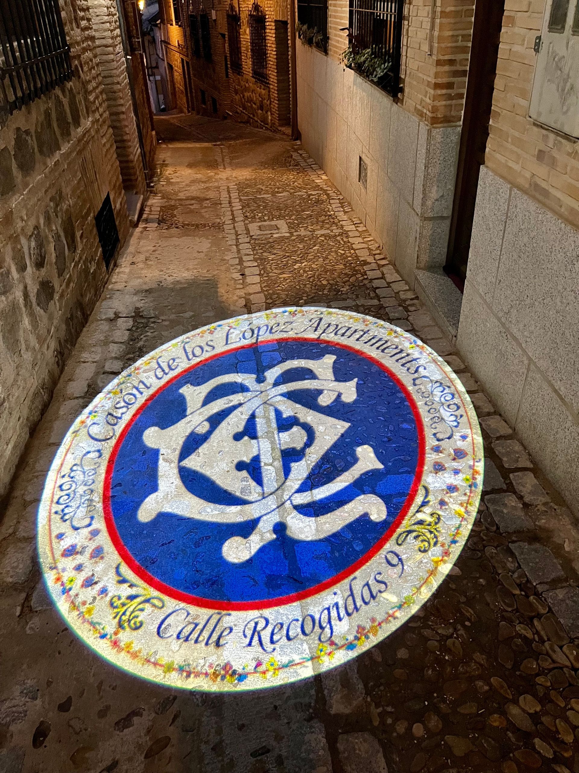 Escena callejera con un emblema azul y blanco en el suelo, en un callejón, Calle Recoletos, España.