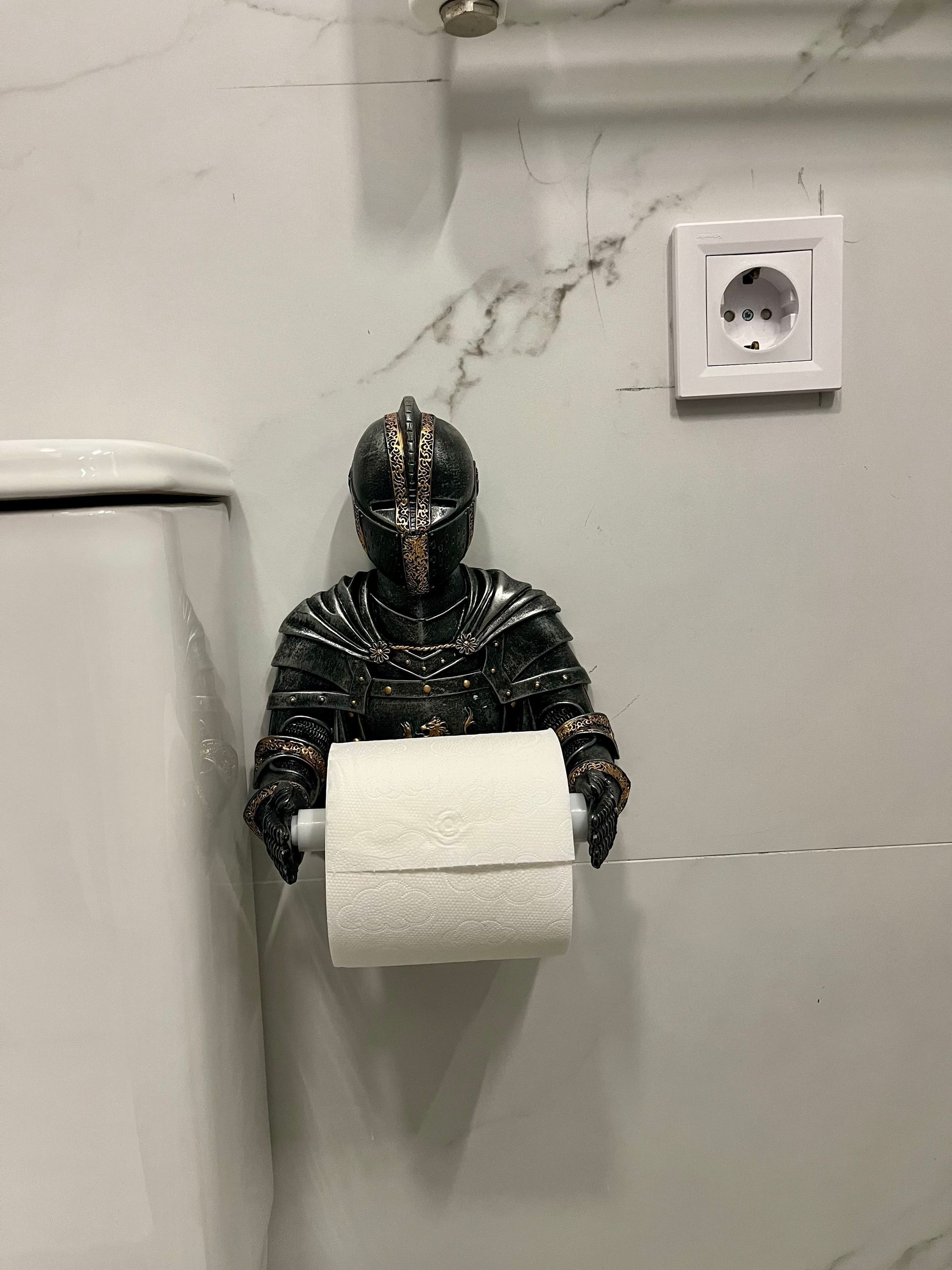 Portarrollos de papel higiénico con forma de caballero, montado en una pared de baño de mármol.