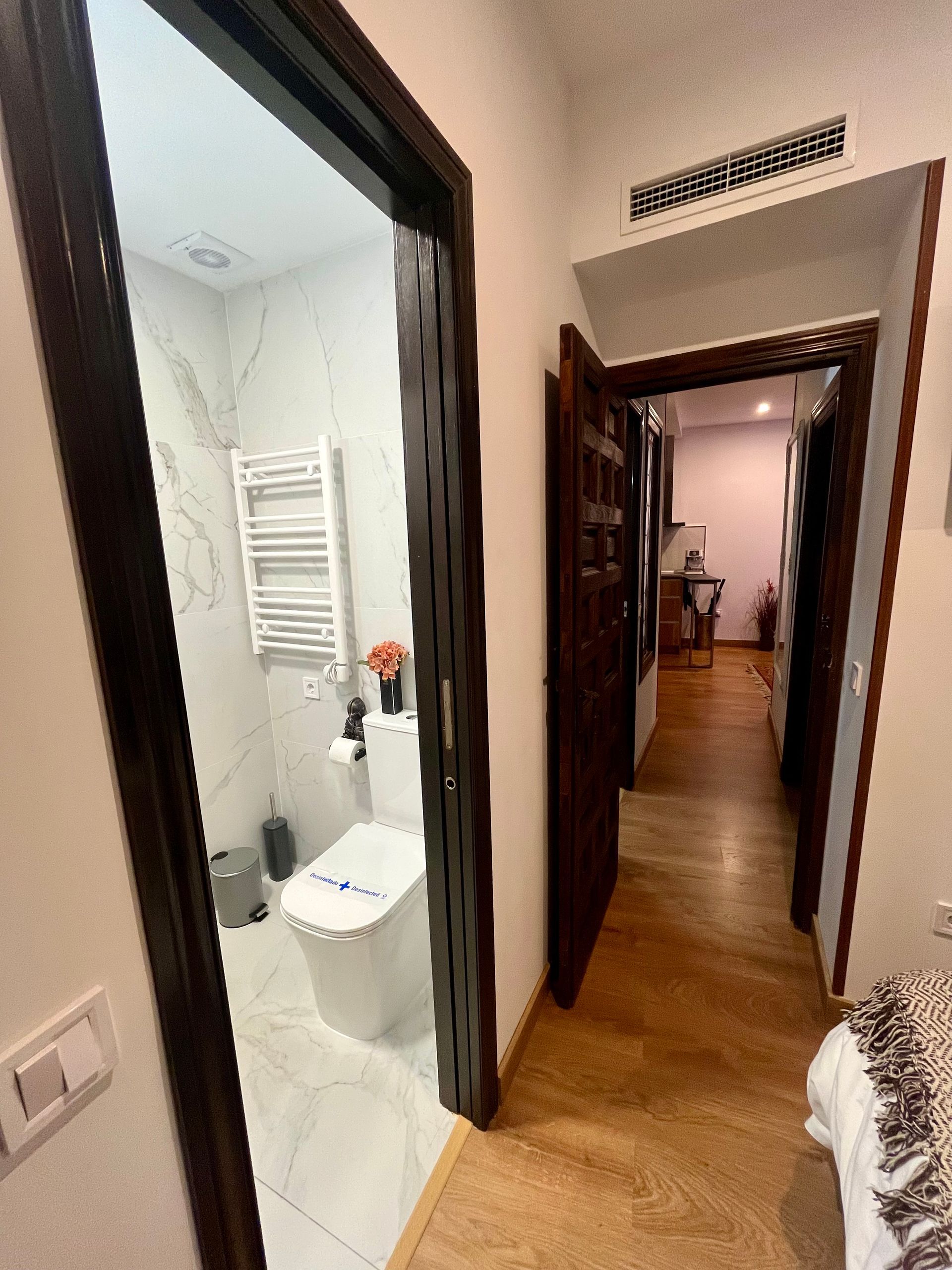 Pasillo con puertas oscuras, baño con azulejo blanco y WC visible.