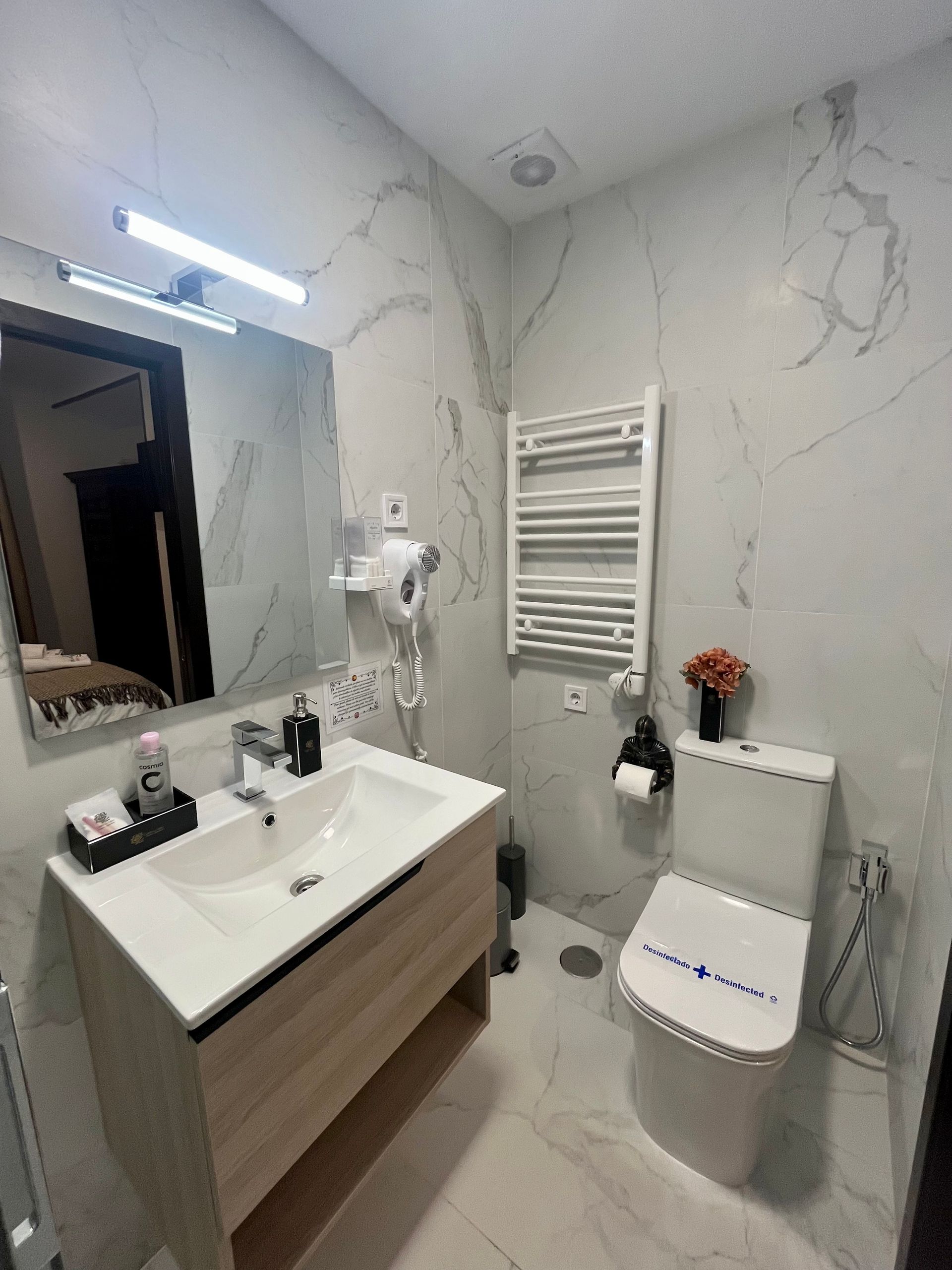 Baño moderno con paredes de mármol blanco, inodoro, lavabo y calentador de toallas.