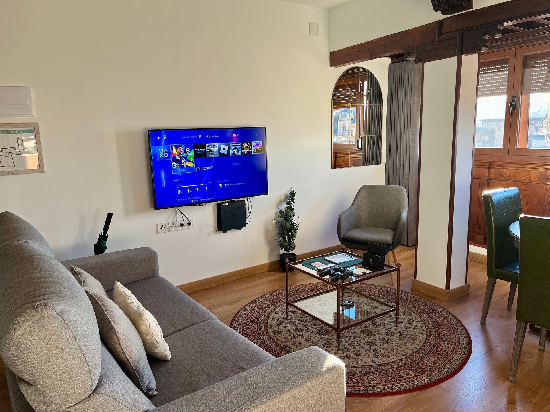 Acogedora sala de estar con televisor, sofá y alfombra redonda. Una silla junto a una pequeña mesa de cristal.