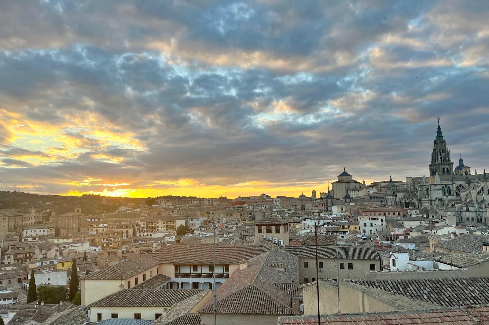 Puesta de sol sobre Matera, Italia, con edificios de piedra, la torre de la catedral y un cielo dramático y nublado.