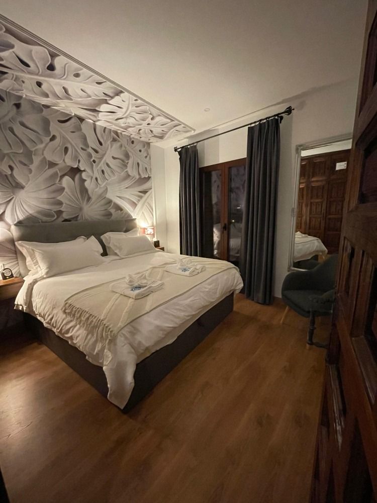 Dormitorio con cama grande, mural de pared floral, cortinas oscuras y piso de madera.