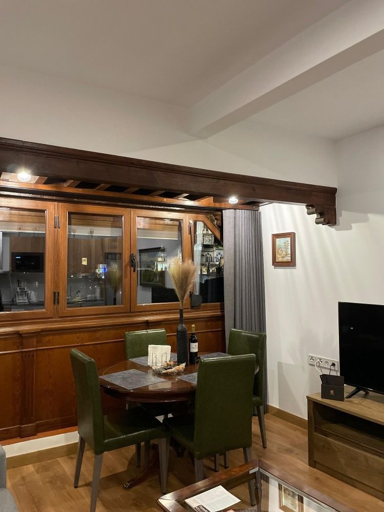 Comedor con mesa redonda, sillas verdes, viga de madera, mueble y TV.