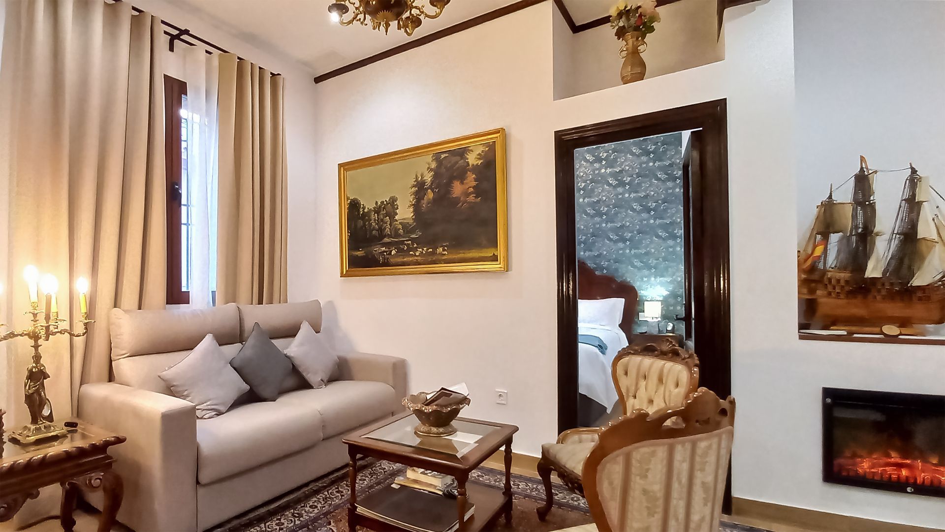 Acogedora sala de estar con sofá, sillón, cuadro, chimenea y puerta de entrada a un dormitorio.