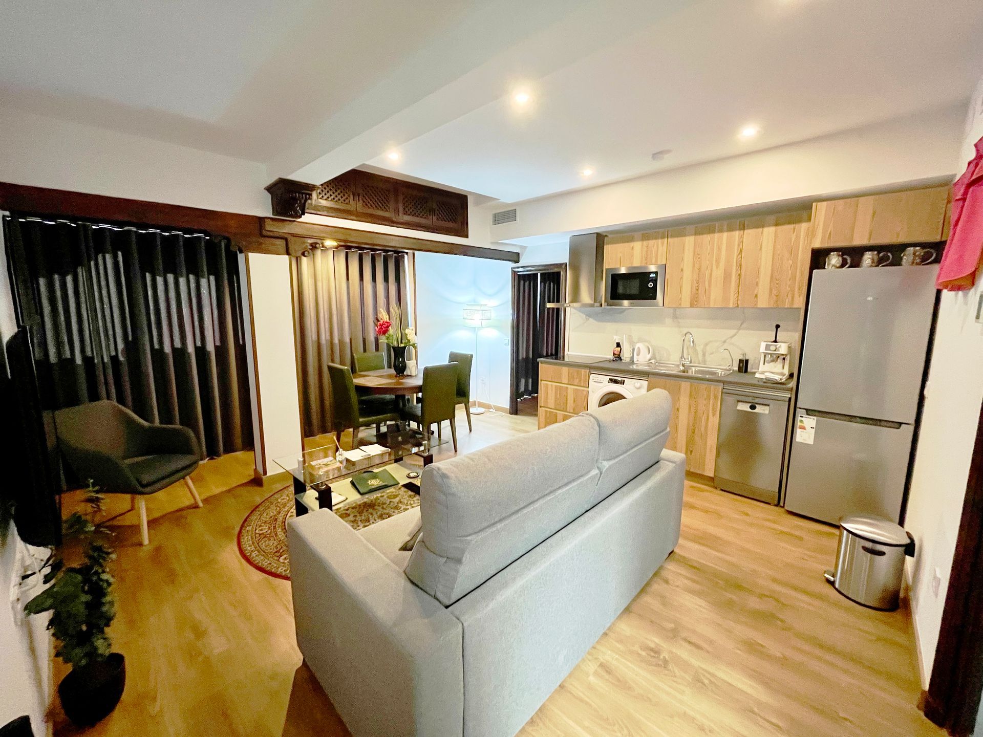 Acogedor interior de apartamento: sala de estar con sofá, mesa de comedor, cocina con gabinetes de madera y electrodomésticos de acero inoxidable.
