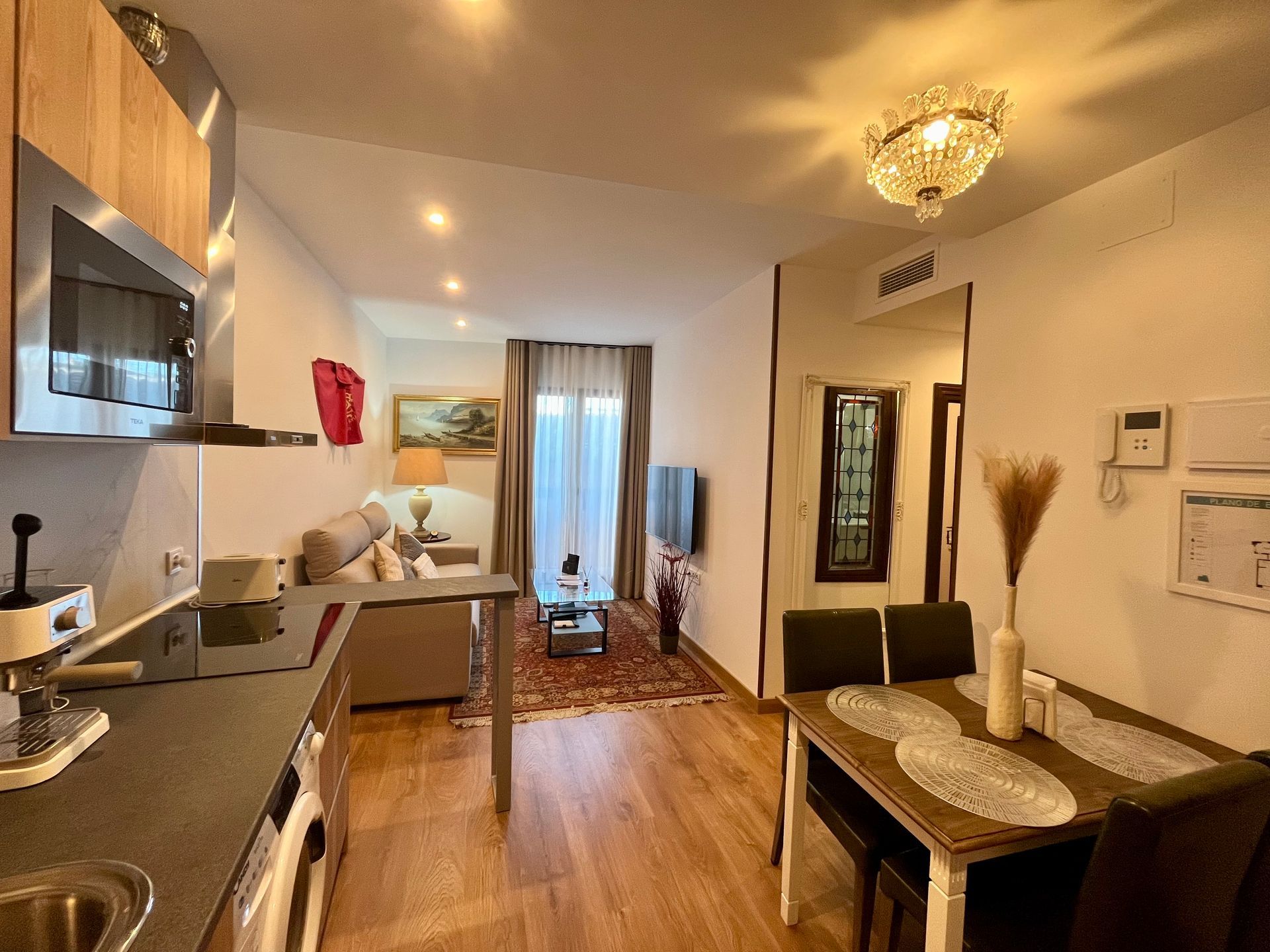 Acogedor interior de apartamento con cocina, mesa de comedor, sala de estar y lámpara de araña.