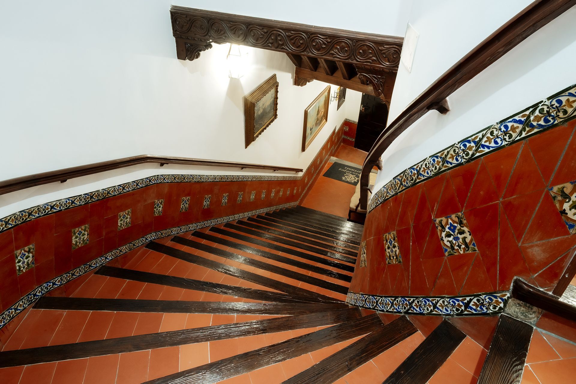 Escalera con contrahuellas de azulejos rojos y peldaños de madera oscura. Azulejos decorativos de cerámica en los laterales.