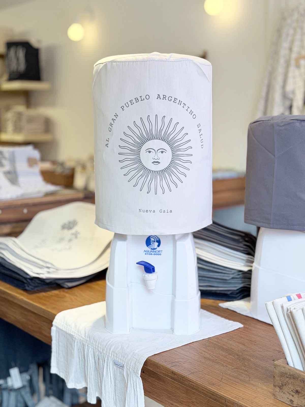 Lámpara cilíndrica blanca con diseño de cara de sol sobre un mostrador de madera en una tienda boutique.