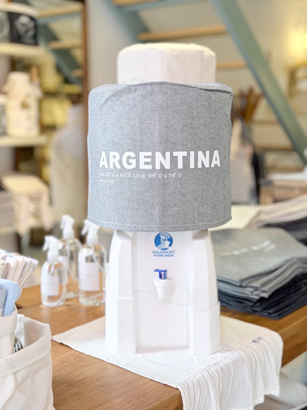 Enfriador de botellas gris argentino sobre un dispensador blanco en un escaparate de tienda.