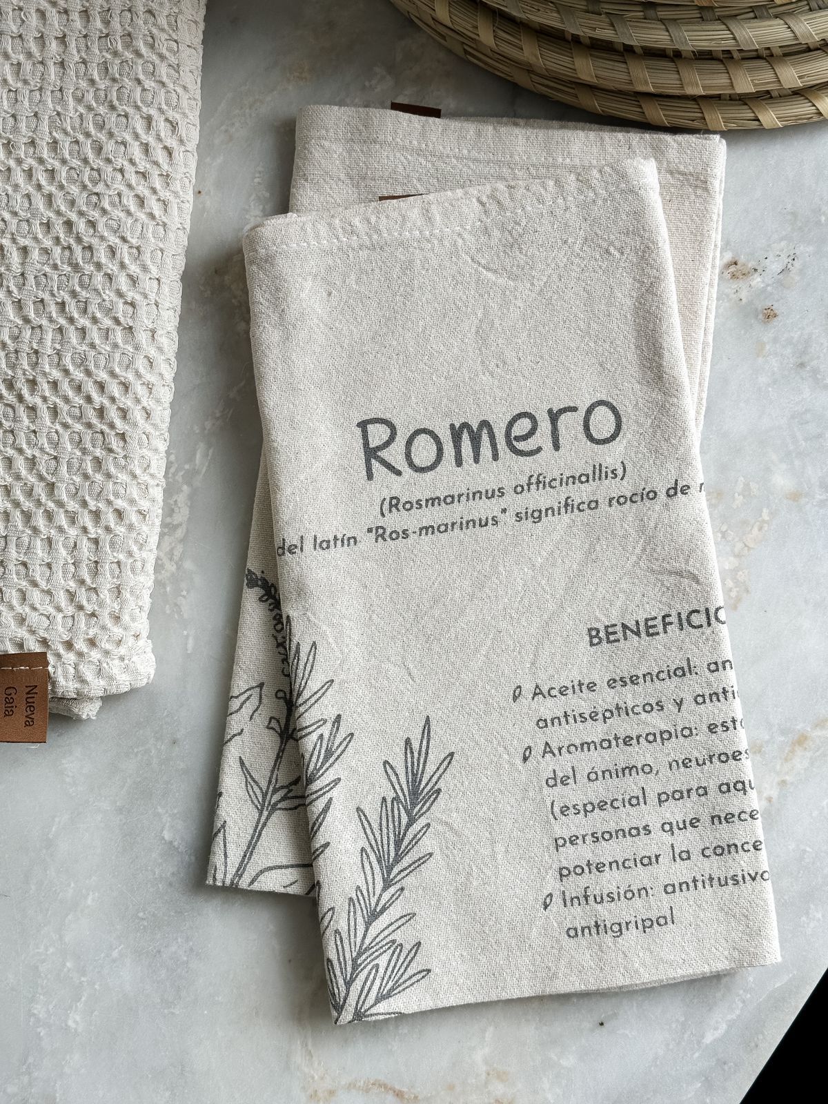 Dos paquetes de papel Romero de color beige con estampado botánico negro sobre una superficie de tela texturizada.