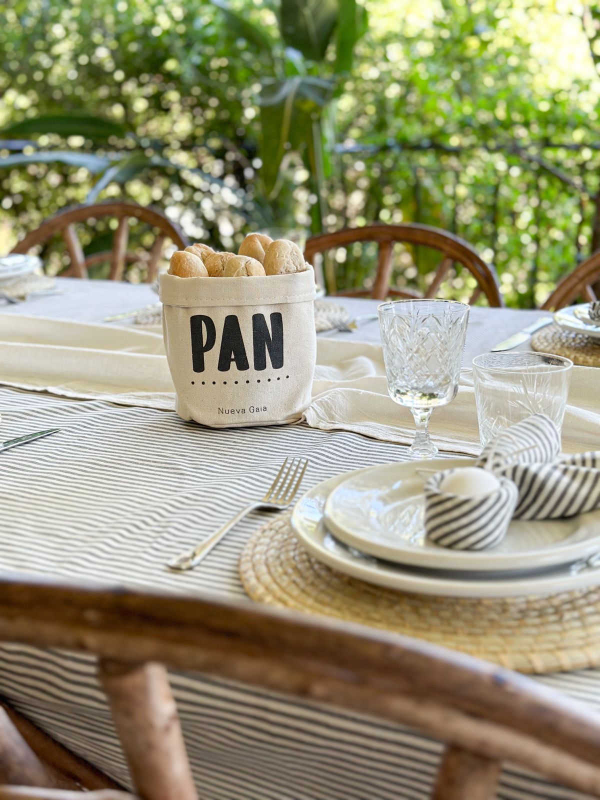 Juego de mesa de comedor para exteriores con cesta de pan PAN, platos, vasos y servilletas a rayas sobre un mantel a cuadros.