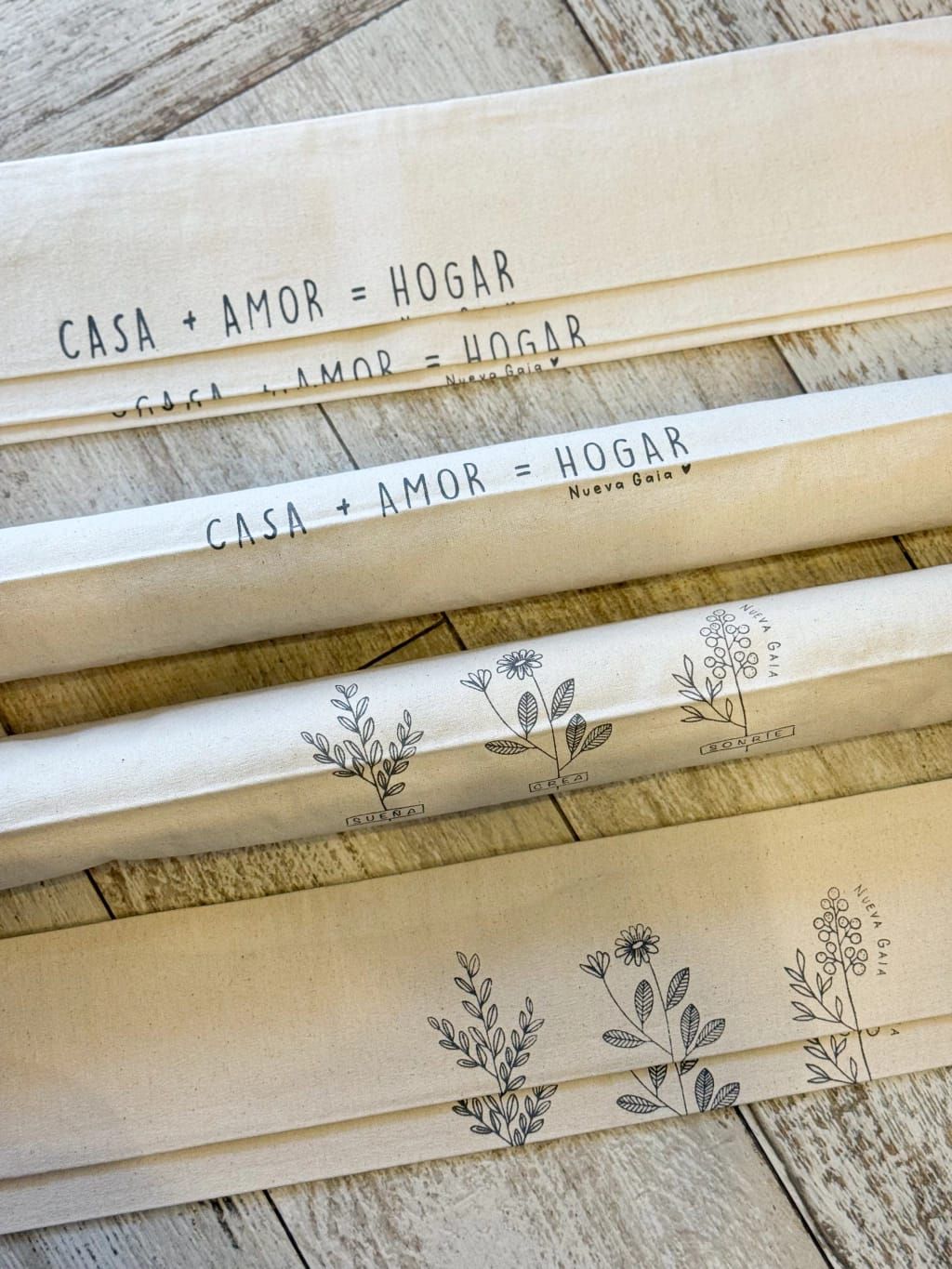 Rollos de tela color crema apilados con estampados botánicos y el texto “CASA + AMOR + HOGAR” en las etiquetas.