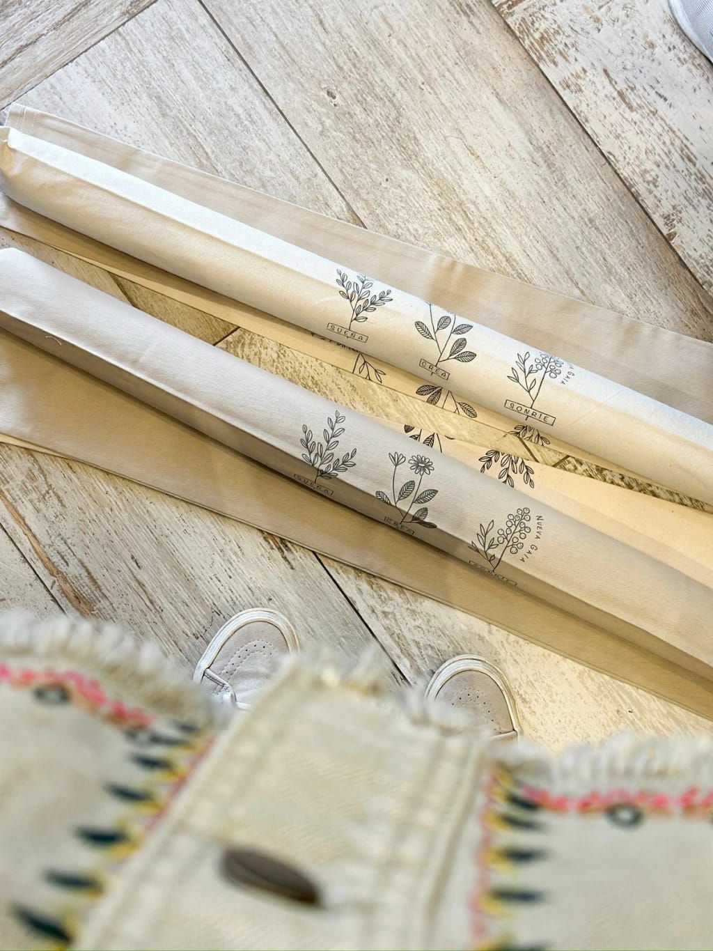 Rollos de tela color crema apilados con estampados botánicos y el texto “CASA + AMOR + HOGAR” en las etiquetas.