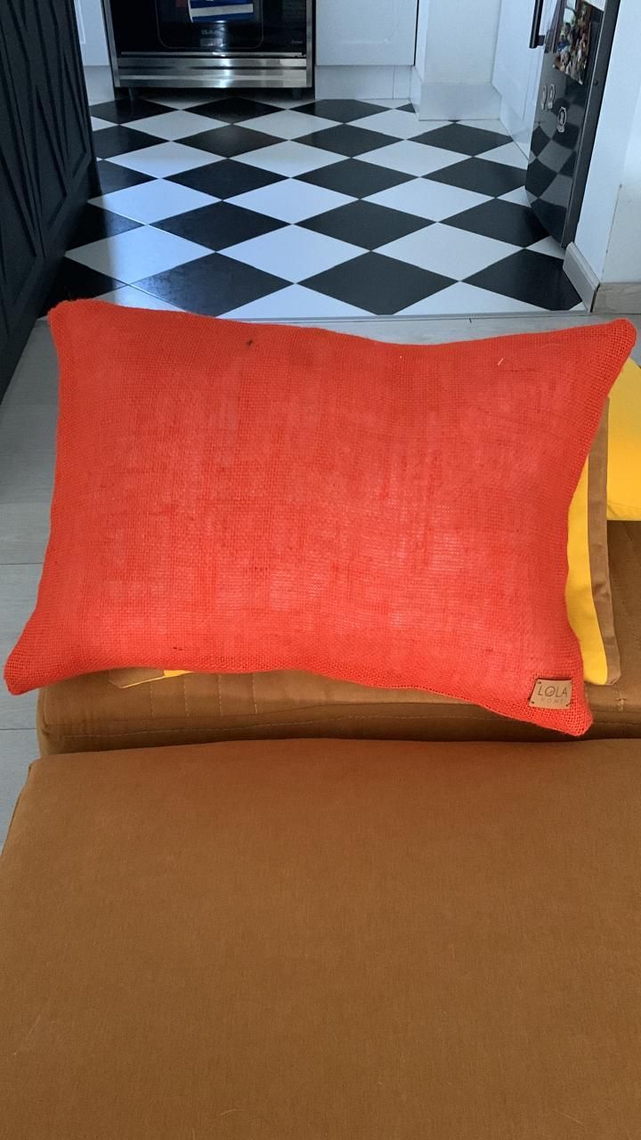 Sofá marrón con un cojín rojo frente a un pasillo con suelo de baldosas a cuadros blancas y negras.